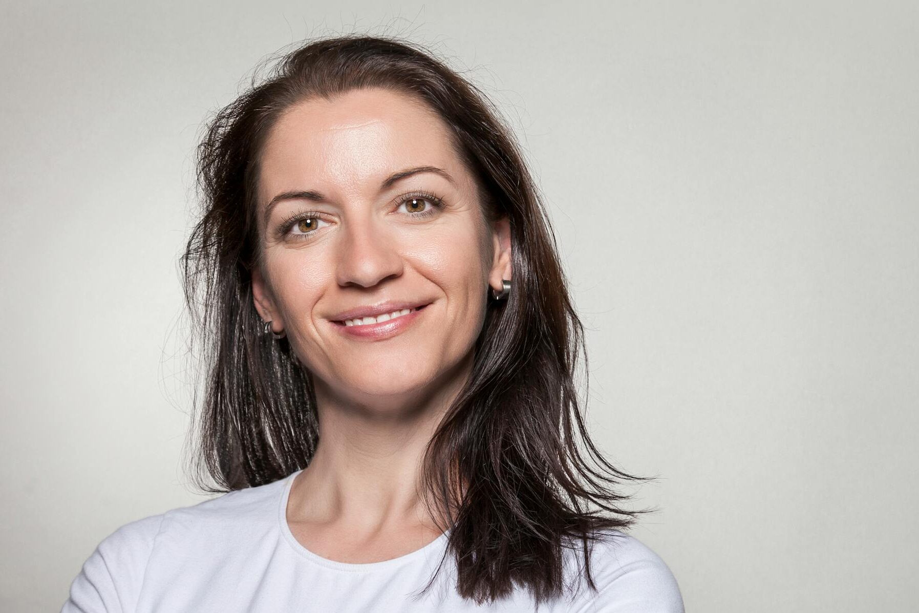 Portrait of a confident woman smiling with arms crossed, wearing a white t-shirt on a gray background.